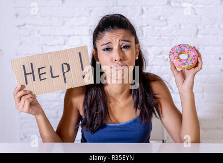 Junge besorgt Latin Frau Gefühl versucht und schuldig, Schokolade und Donuts um Hilfe zu bitten, in der Diät Kalorien Zucker Ernährung Essen ein Stockfoto