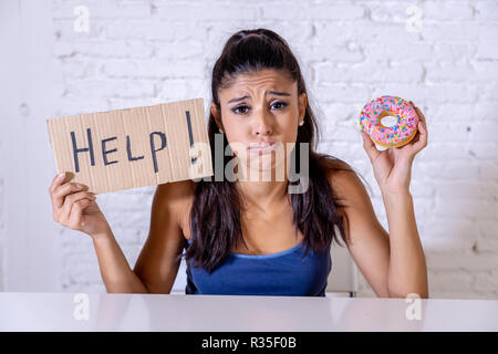 Junge besorgt Latin Frau Gefühl versucht und schuldig, Schokolade und Donuts um Hilfe zu bitten, in der Diät Kalorien Zucker Ernährung Essen ein Stockfoto