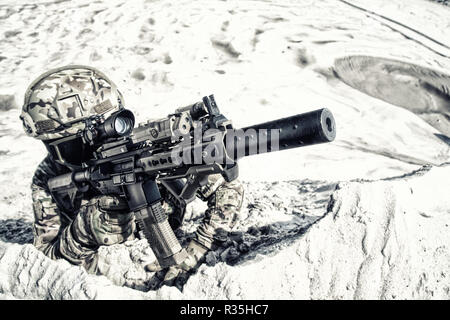 Airsoft Spieler in militärische Tarnung uniform, Helm und Brille in Sand und mit dem Ziel der optischen Anblick auf den Militärdienst Gewehr oder Karabiner realistisch Stockfoto