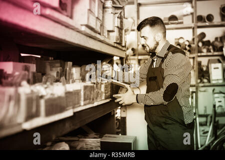 Lächeln Fröhlicher positiver Mann Arbeiter gehen durch Sanitärtechnik Details in der Werkstatt Stockfoto