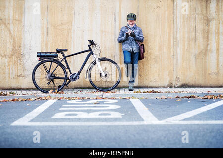 Active Senior Mann mit electrobike stehen draußen in der Stadt, mittels Smartphone. Stockfoto