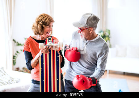 Senior Paar mit Boxhandschuhen und longboard Spaß zu Hause haben. Stockfoto