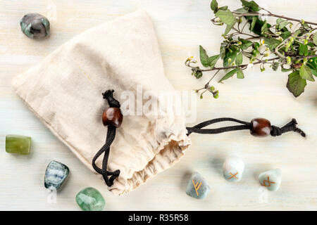 Runen, Steine mit Symbolen in Wicca und andere Magie und für Weissagung benutzt, warf aus der Tasche auf einem hellen Hintergrund mit Kristallen Stockfoto