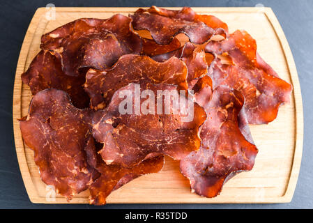 In dünne Scheiben geschnitten und getrocknet geräucherten Schinken auf Eiche Fach kleine Kristalle von Salz auf das Fleisch sichtbar. Stockfoto