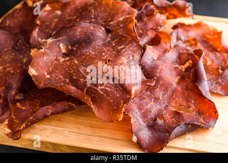 In dünne Scheiben geschnitten und getrocknet geräucherten Schinken auf Eiche Fach kleine Kristalle von Salz auf das Fleisch sichtbar. Stockfoto