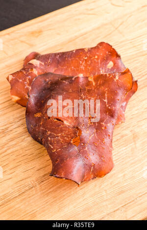In dünne Scheiben geschnitten und getrocknet geräucherten Schinken auf Eiche Fach kleine Kristalle von Salz auf das Fleisch sichtbar. Stockfoto