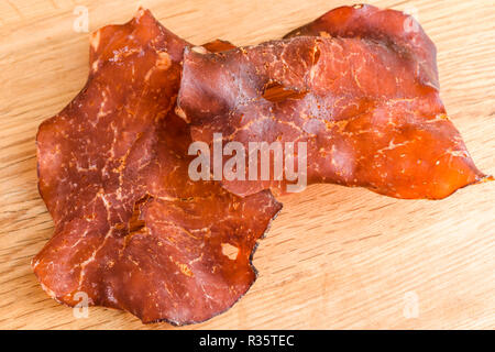 In dünne Scheiben geschnitten und getrocknet geräucherten Schinken auf Eiche Fach kleine Kristalle von Salz auf das Fleisch sichtbar. Stockfoto