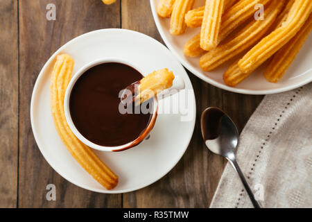 Traditionelle spanische Churros mit heißer Schokoladensauce auf einem rustikalen Holztisch. Ansicht von oben Stockfoto