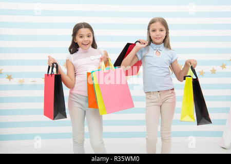 Mädchenhafte Glück. Die Kinder glücklich tragen Bündel Pakete. Einkaufen mit beste Freundin Konzept. Mädchen wie einkaufen. Die Kinder glücklich kleine Mädchen halten Einkaufstaschen. Viel Spaß beim Shoppen mit der besten Freundin oder Schwester. Stockfoto