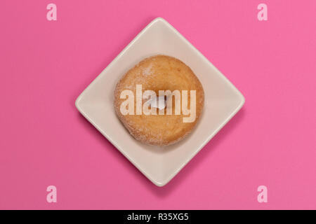 Zucker überzogen Donut auf einem weißen Teller mit rosa Hintergrund Stockfoto