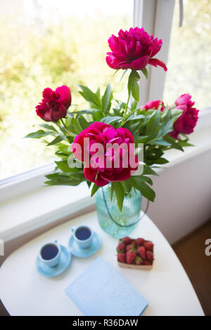 Erdbeere, Buch, Blumenstrauß aus schönen Pfingstrosen und zwei Tassen Kaffee auf weißen Tisch Stockfoto