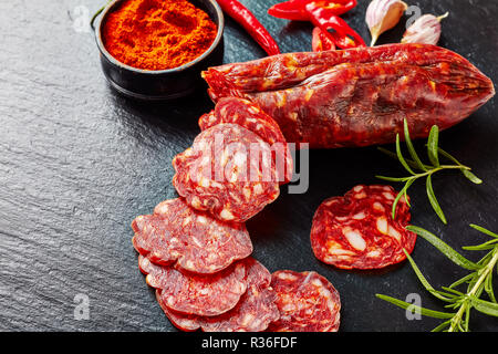 Chorizo Wurst in Scheiben geschnitten auf schwarzem Schiefer Platte mit geräucherter Paprika, Chili und frischem Rosmarin, Ansicht von oben, close-up Stockfoto