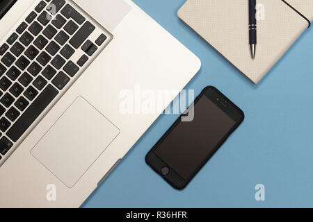 Laptop, Smartphone und eine Notiz Buch auf einem blauen Schreibtisch, flach. Stockfoto