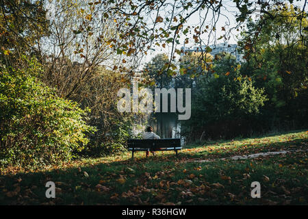 London, UK, 27. Oktober 2018: die Person, die auf einer Bank sitzen, entspannen Sie am Teich in Hampstead Heath. Hampstead Heath umfasst 320 Hektar eines von Londons Stockfoto