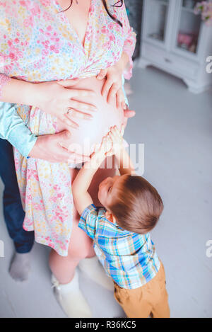 Ein kleiner Junge, und wartet auf seine Schwester, sanft berührt seine Mutter Bauch Stockfoto