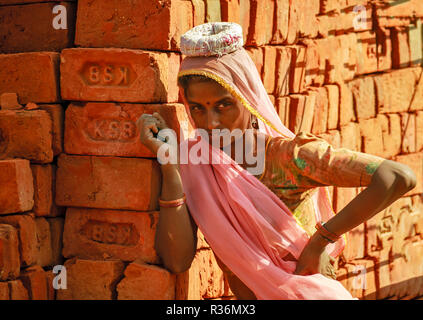 RAJASTHAN INDIEN JUNGE FRAU, DIE VON SCHWEREN LASTEN ZIEGELSTEINE AUF DEM KOPF Stockfoto