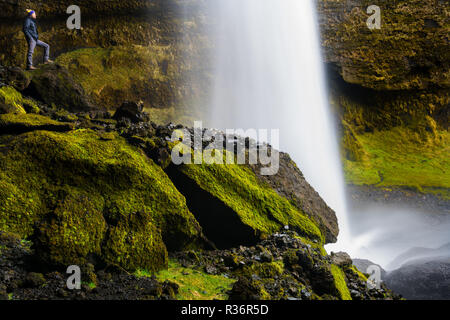 Person steht hinter der faszinierenden Kvernufoss Wasserfall in Island. Stockfoto