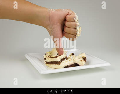 Weibliche Hand mit dem Finger nach unten. Daumen nach unten auf den Hintergrund des Kuchens. Nicht lecker Kuchen. Abneigung Kuchen. Gestreifte Schokolade Kuchen. Konzept ist im Gegensatz zu Stockfoto