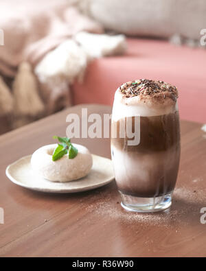 Ein Glas Milch Schokolade Frappe mit Schlagsahne auf Holztisch mit Blur Weißzucker Donut auf dem Tisch Stockfoto