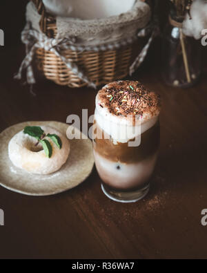 Schokolade Milchshake mit Kaffee und bunten Streuseln Zucker als Topping und Unschärfe Donut und Minzeblatt auf hölzernen Tisch im Cafe Stockfoto