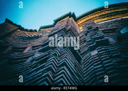 Hintergrund von gekrümmten alten Orange brick wall mit blauem Himmel und Sonne Licht im Hintergrund. Keine Menschen. Stockfoto