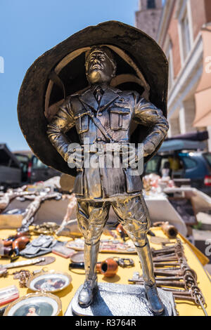 Lustiges Bild von einem Helm auf einer kleinen Mussolini stahl Statue auf einem Tisch mit Oldtimer und alte Erinnerungsstücke Objekte an einer Straße Flohmarkt abgewürgt. Kein Mitarbeiter Stockfoto