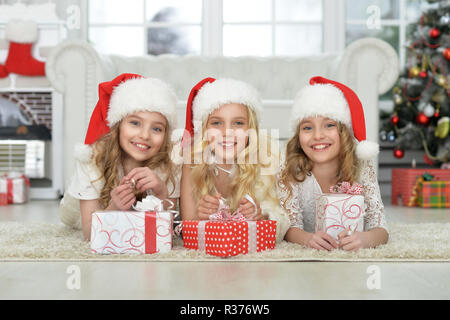 Süße kleine Mädchen in Santa Hüte auf dem Boden liegend Stockfoto