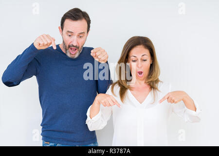 Schönen mittleren Alter Paar in Liebe über isolierte Hintergrund nach unten zeigt mit Fingern zeigen Werbung, überraschte Gesicht und offenem Mund Stockfoto