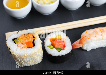 Typische asiatische Küche auf schwarze Küche Schiefer. Fischsauce in kleine weiße Schüssel. Stäbchen. Sushi - futomaki und Nigiri. Stockfoto