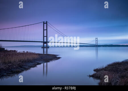 Die Humber Bridge ist wie die untergehende Sonne taucht unter der Wolke auf einem kalten Wintertag am Nachmittag bei Flut am Barton auf Humber beleuchtet Stockfoto