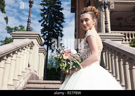 Braut in einem weißen Kleid mit einem schönen wedding bouquet auf einer Marmortreppe in einer alten Burg. Hochzeit Zubehör. Hochzeit Konzept. Stockfoto