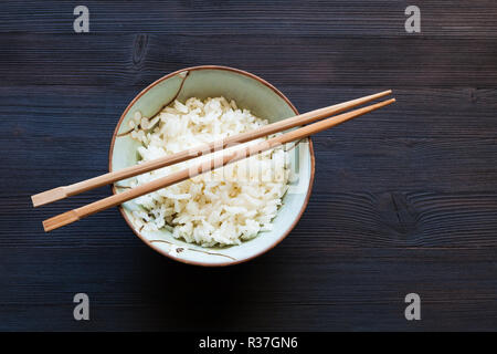 Blick von oben auf die Stäbchen über gekochten Reis in der Schüssel auf dunklen Holzplatte mit Copyspace Stockfoto