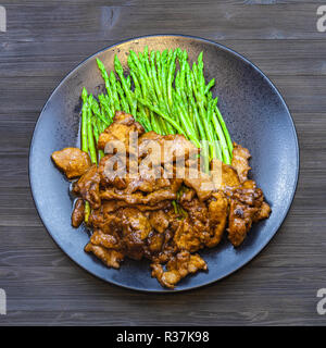 Chinesische Küche Teller - oben Ansicht von Rindfleisch gebraten in Sojasauce mit grünem Spargel auf schwarze Platte auf dunklen Tabelle Stockfoto