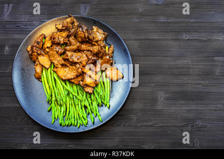 Chinesische Küche Teller - Ansicht von oben von Rindfleisch gebraten in Sojasauce mit grünem Spargel auf schwarze Platte auf dunklen Holzplatte mit Copyspace Stockfoto
