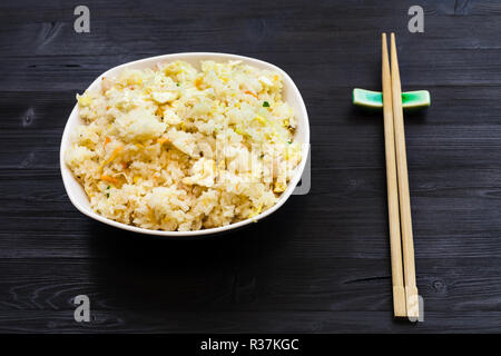 Chinesische Küche Teller - Serviert Portion gebratener Reis mit Garnelen, Gemüse und Eier (Yangzhou) Reis mit Essstäbchen auf dunklen Holztisch Stockfoto