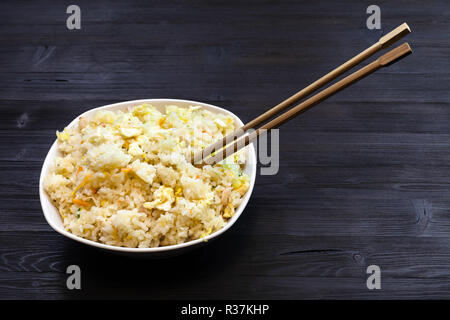 Chinesische Küche Teller - Schüssel mit gebratener Reis mit Garnelen, Gemüse und Eier (Yangzhou) Reis mit Essstäbchen auf dunklen Holztisch Stockfoto