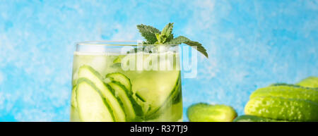 Gurken Wasser mit Minze ist beliebt detox drink Glas von antioxidativen Infusion mit Scheiben von Gemüse am Küchentisch und blauer Hintergrund Stockfoto