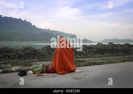 Ein pelgrim Neben den heiligen Ganges Fluss in der Dämmerung sitzen. Rishikesh, Indien Stockfoto