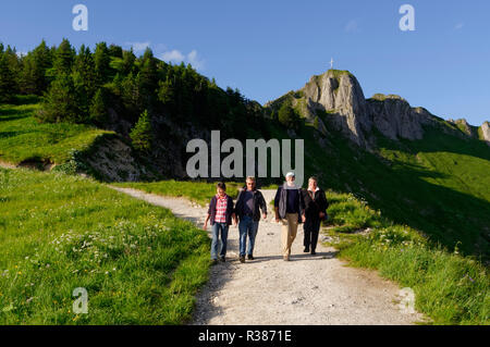 Wanderer auf dem Tegelberg bei Schwangau, im Hintergrund das Gipfelkreuz auf dem Brandnerschrofen, Ammergauer Alpen, Bayern, Deutschland Stockfoto