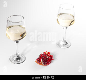 Gebrochene Granatapfel liegt auf einem weißen Teller. Zwei Gläser Weißwein. Weißer Hintergrund. Stockfoto