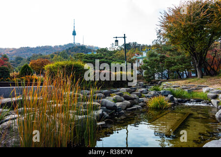 Namsan Tower von Namsangol Hanok Village, Seoul, Südkorea. Ein schöner Garten und Strom befindet sich im Vordergrund mit Bäumen im Herbst Farben Stockfoto