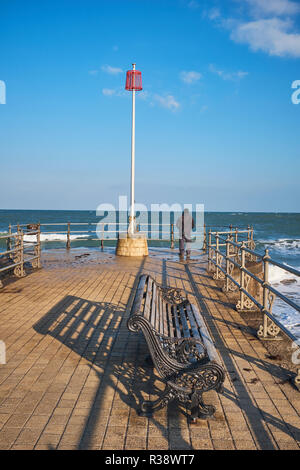 Eine Ansicht von hinten von einem Mann auf seinem eigenen ständigen Blick über den Englischen Kanal am Ende einer Anlegestelle in Swanage, Dorset, England, Großbritannien Stockfoto