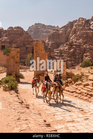 Touristische und Führer auf dromedare bei Temenos Tor, Zentrum von Petra, die antike römische Straße neben Ruinen von Petra Stockfoto