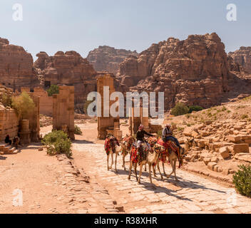 Touristische und Führer auf dromedare bei Temenos Tor, Zentrum von Petra, die antike römische Straße neben Ruinen von Petra Stockfoto