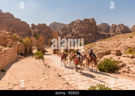 Touristische und Führer auf dromedare bei Temenos Tor, Zentrum von Petra, die antike römische Straße neben Ruinen von Petra Stockfoto