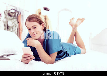 Lächelnde niedliche gender-queer Chillen im Bett, während Sms Stockfoto