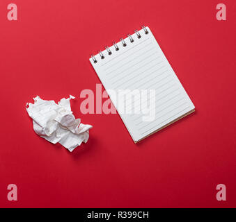 Öffnen Sie Notizbuch mit weißer Bettwäsche und ein zerknittertes Blatt Papier zerrissen auf rotem Hintergrund Stockfoto