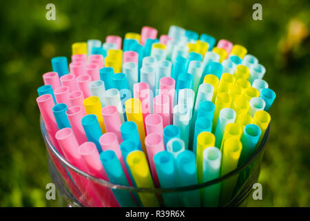 Hellen bunten Cocktail trinken Strohhalme und Röhren zusammen im großen Glas auf grünem Gras Sommer Hintergrund gestellt. Vorbereitung zur Party Stockfoto