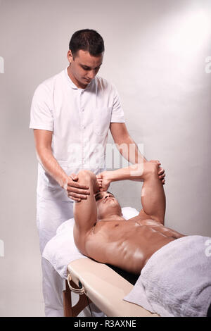 Zwei junge Mann, 20-29 Jahre alt, Sport Physiotherapie drinnen im Studio, Foto schießen. Physiotherapeut stretching muskulösen Arme des Patienten mit den Händen. Stockfoto