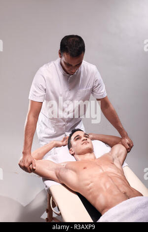 Zwei junge Mann, 20-29 Jahre alt, Sport Physiotherapie drinnen im Studio, Foto schießen. Physiotherapeut stretching muskulösen Arme des Patienten mit den Händen. Stockfoto